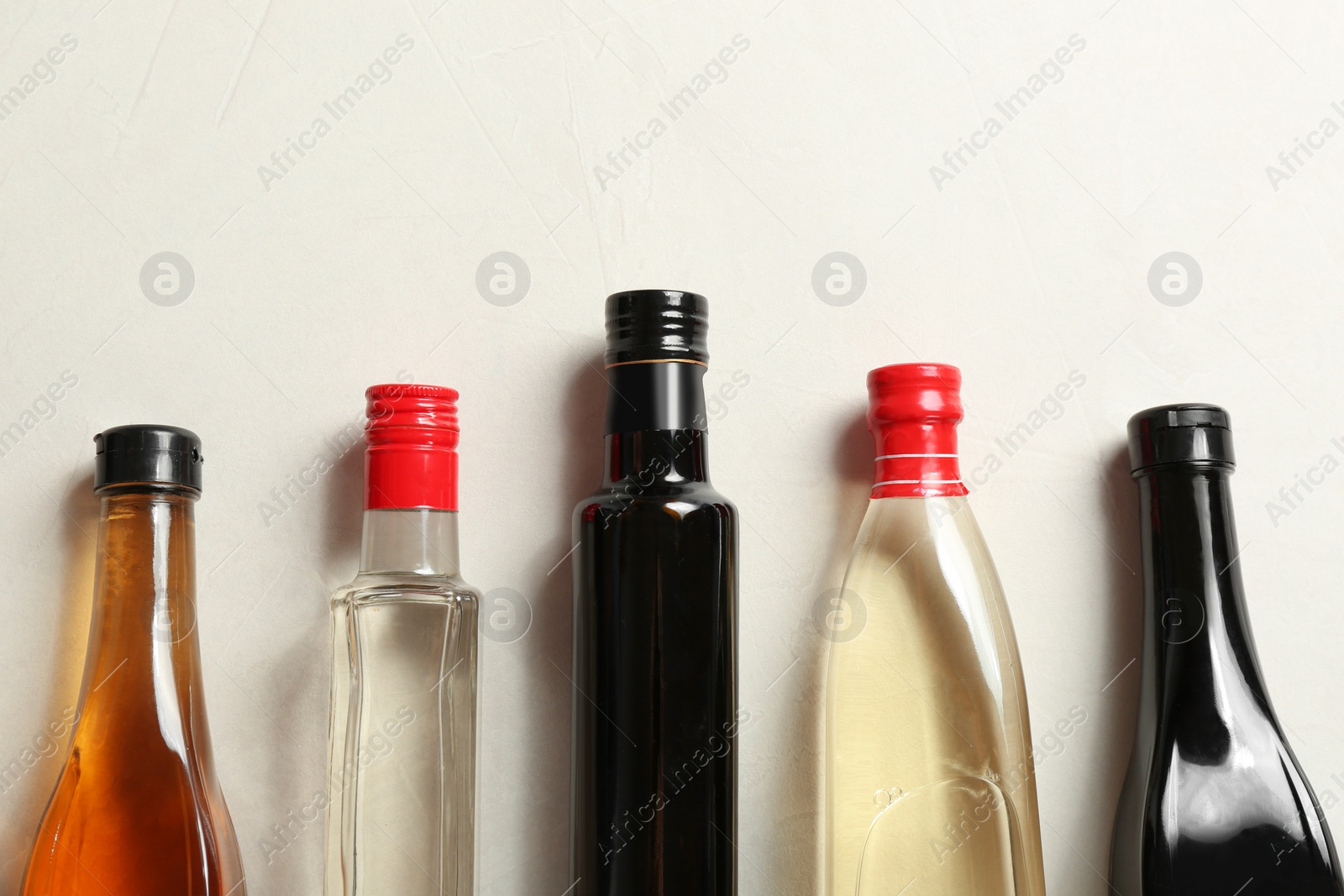 Photo of Flat lay composition with different kinds of vinegar in bottles and space for text on light background