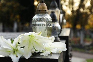 Photo of White lilies and grave lights on granite tombstone outdoors, space for text. Funeral ceremony