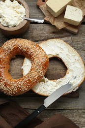 Delicious bagel with tofu cream cheese and knife on wooden table, flat lay