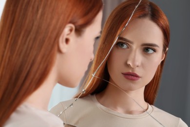 Young woman looking at herself in broken mirror indoors