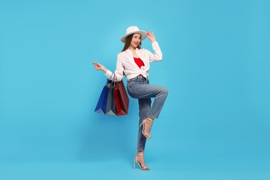 Photo of Stylish young woman with shopping bags on light blue background