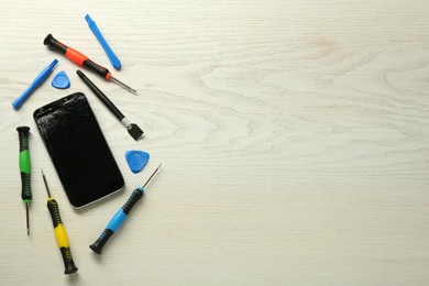 Damaged smartphone and repair tools on wooden background, flat lay. Space for text