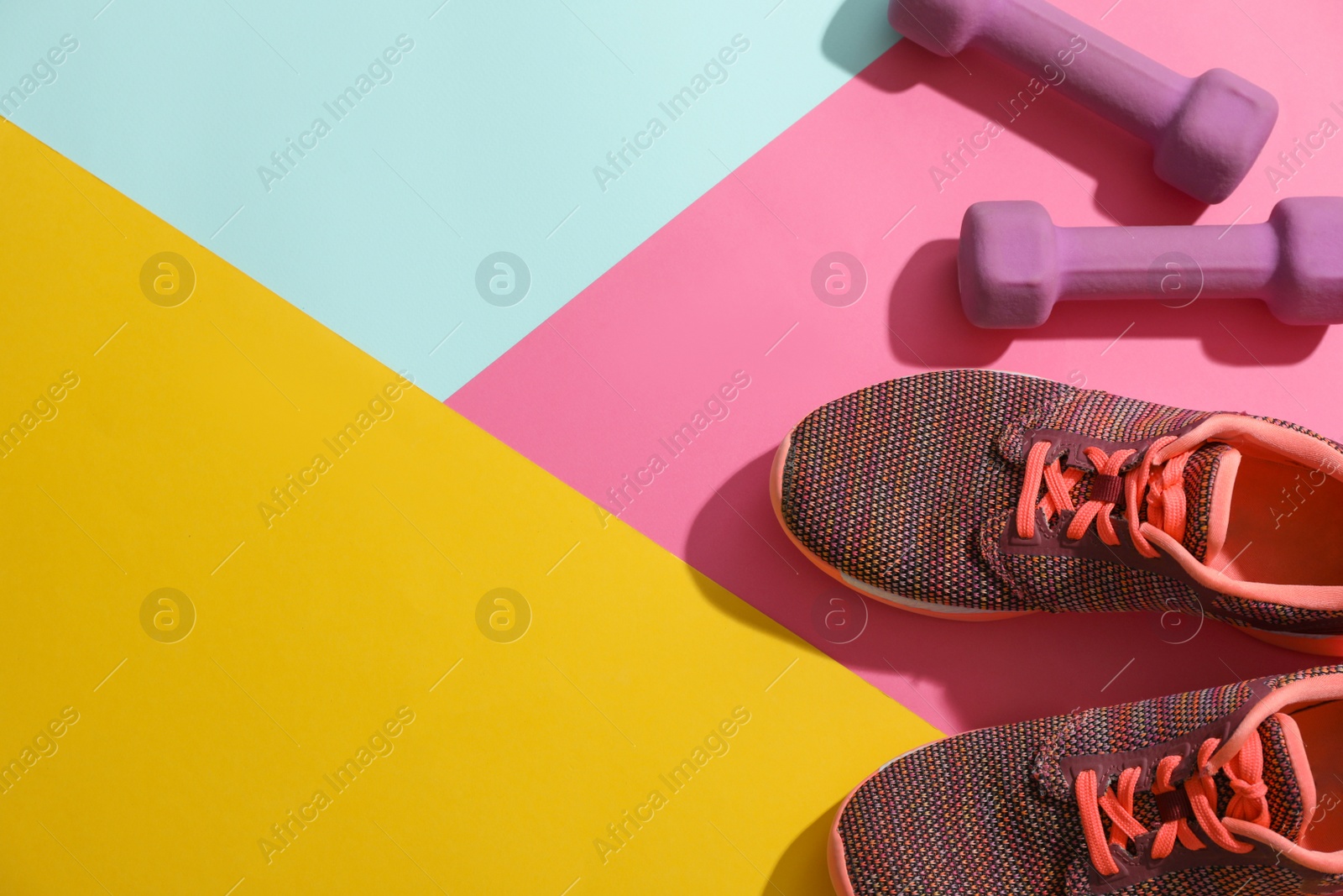 Photo of Dumbbells, sneakers and space for text on color background, flat lay. Physical fitness