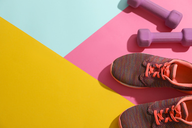Photo of Dumbbells, sneakers and space for text on color background, flat lay. Physical fitness