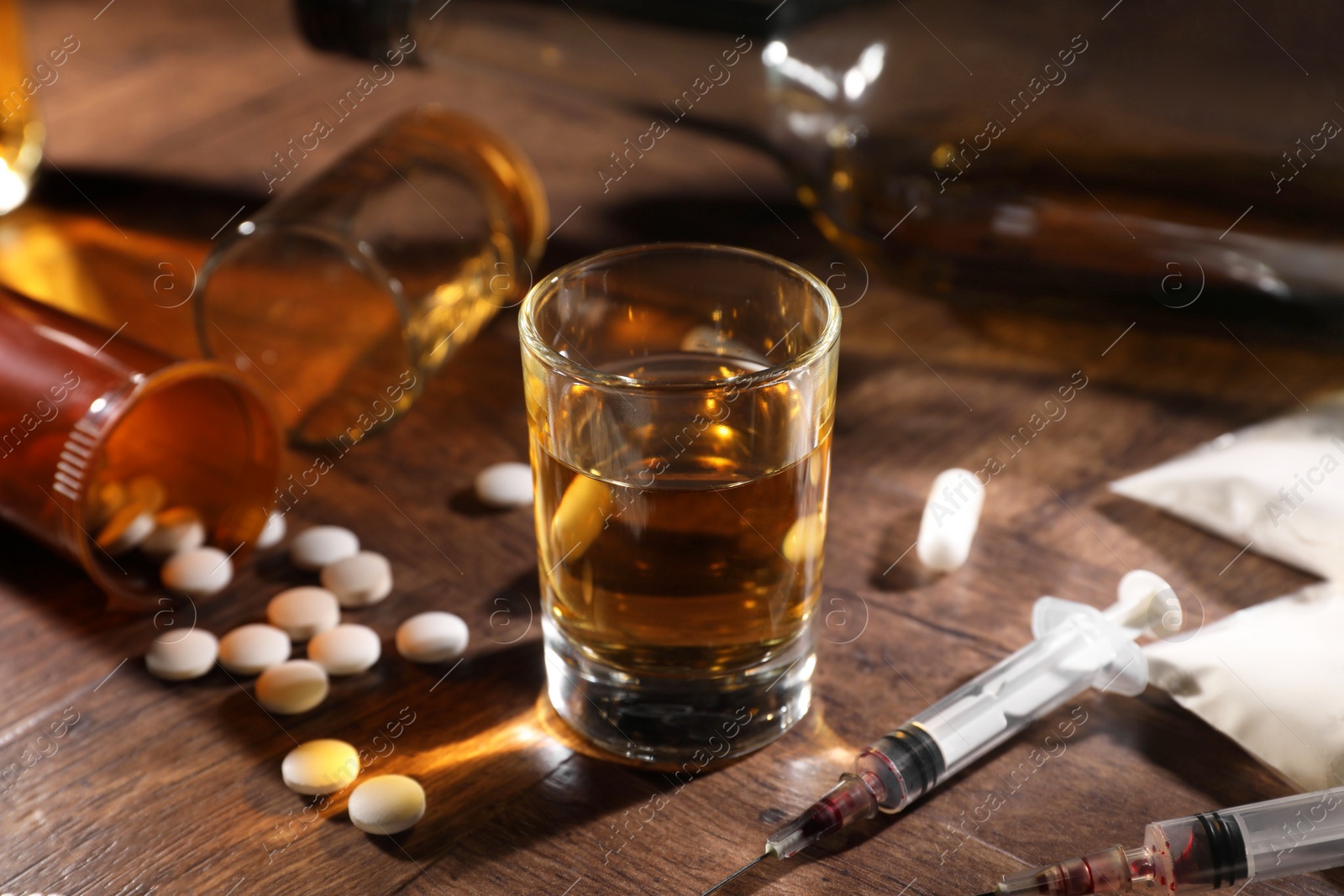 Photo of Alcohol and drug addiction. Whiskey in glass, syringes, pills and cocaine on wooden table