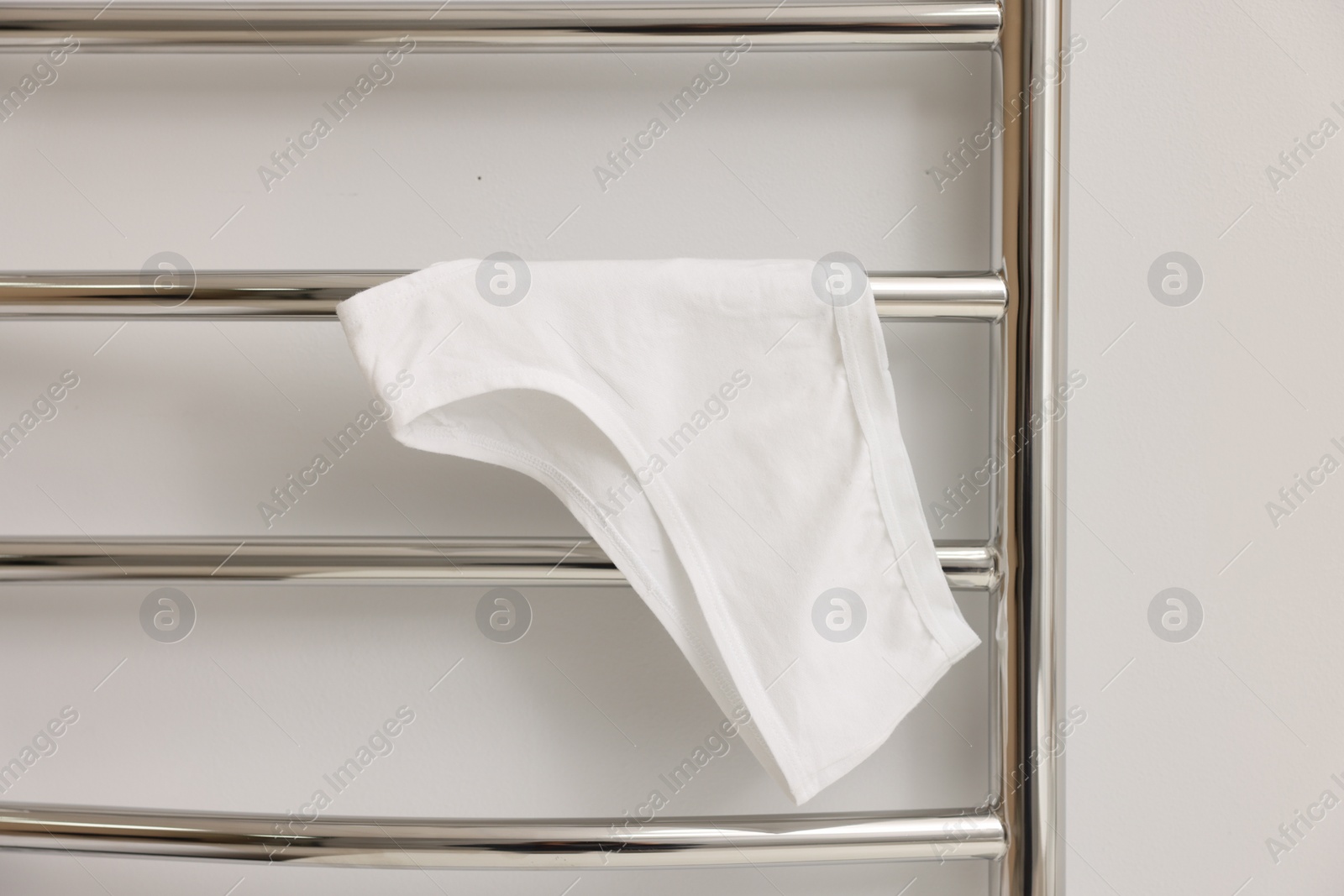 Photo of Heated towel rail with underwear on white wall, closeup