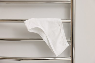 Photo of Heated towel rail with underwear on white wall, closeup