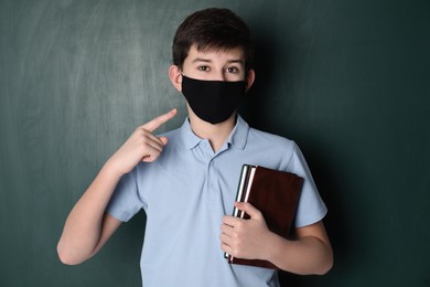 Boy wearing protective mask with books near chalkboard. Child safety