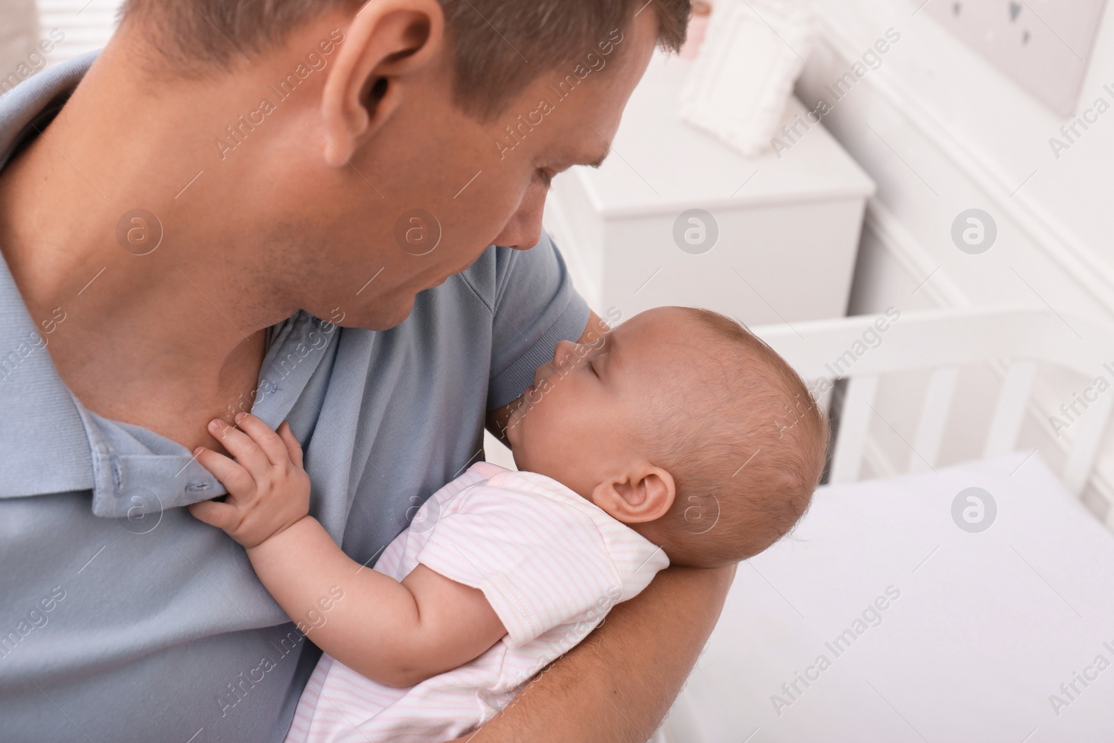 Photo of Happy father with his cute sleeping baby near crib at home