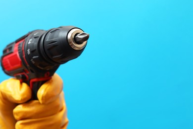 Photo of Handyman holding electric screwdriver on light blue background, closeup. Space for text