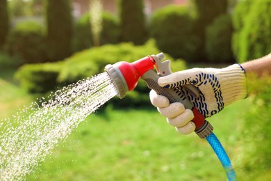 Photo of Man spraying water from hose in garden, closeup