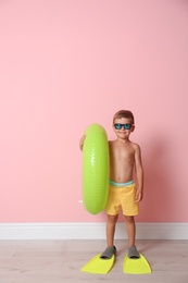 Photo of Cute little boy with inflatable ring wearing flippers near color wall