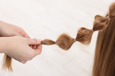 Photo of Professional stylist braiding woman's hair on blurred background, closeup