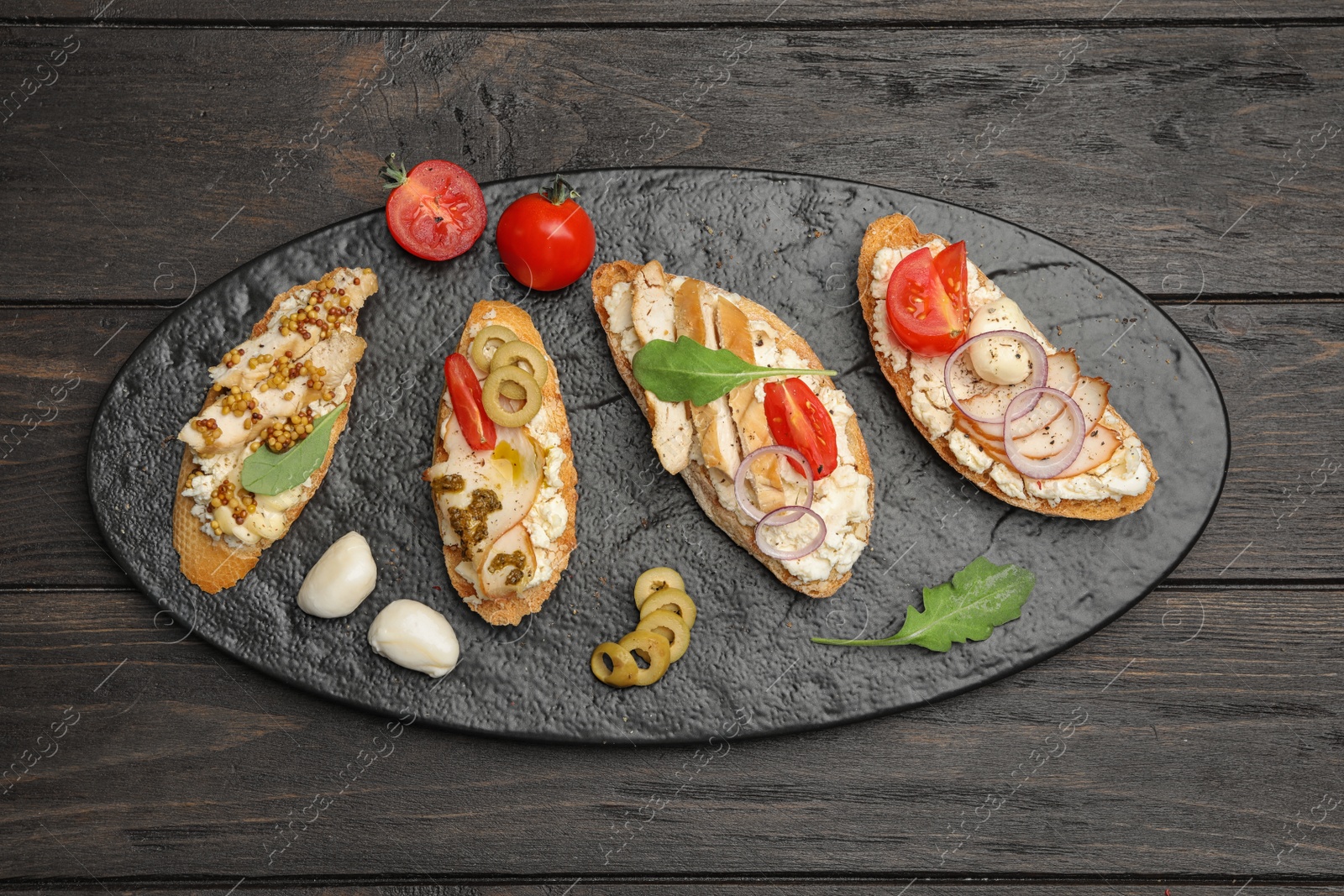 Photo of Slate plate of delicious chicken bruschettas on wooden table, top view