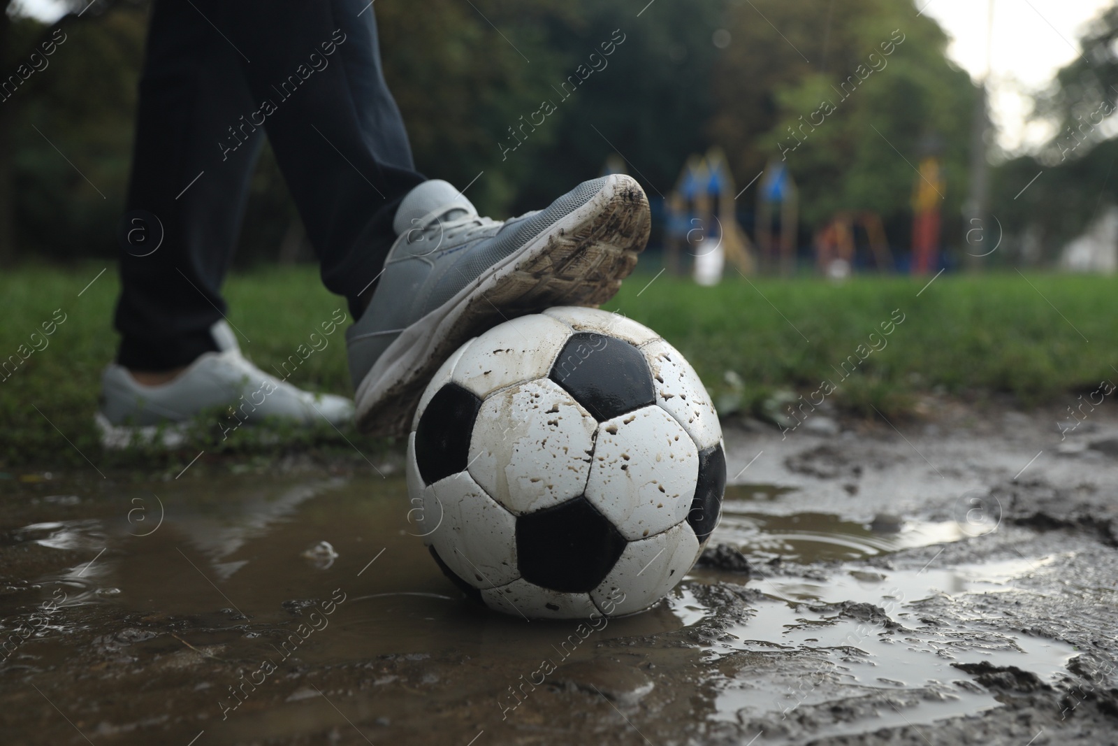 Photo of Man with dirty soccer ball in puddle outdoors, closeup