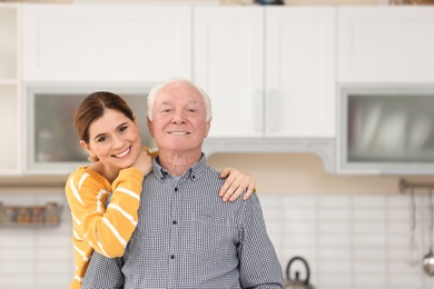 Photo of Elderly man with female caregiver in kitchen. Space for text