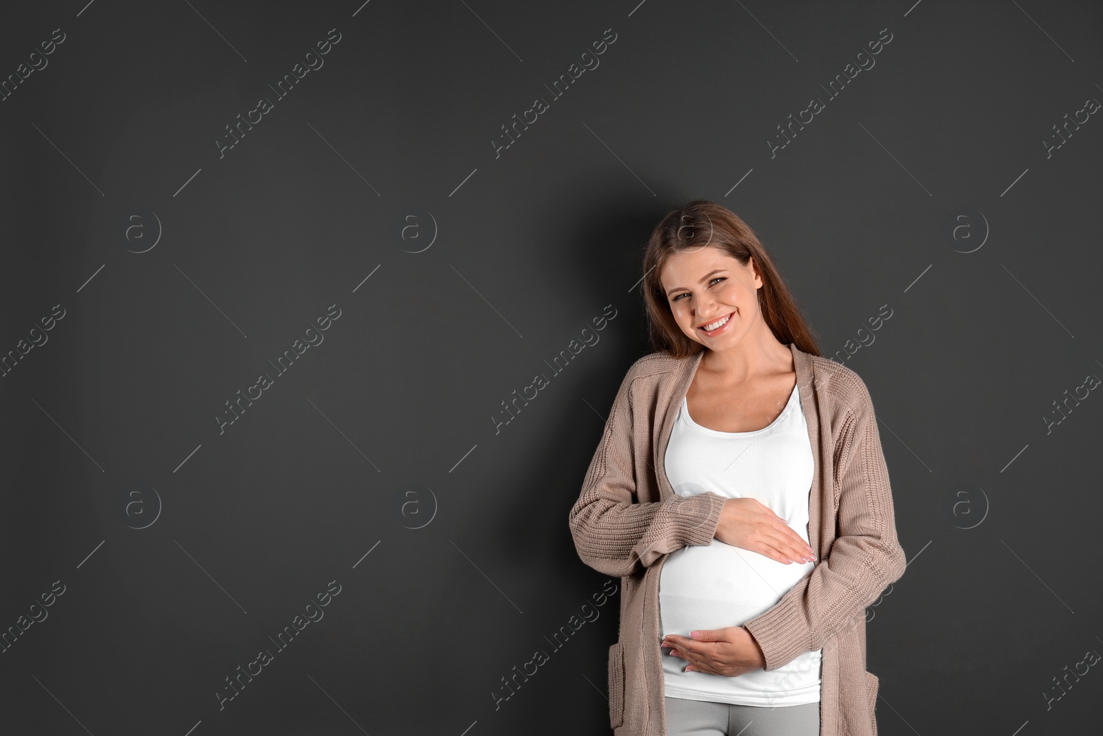 Photo of Young pregnant woman on grey background. Space for text