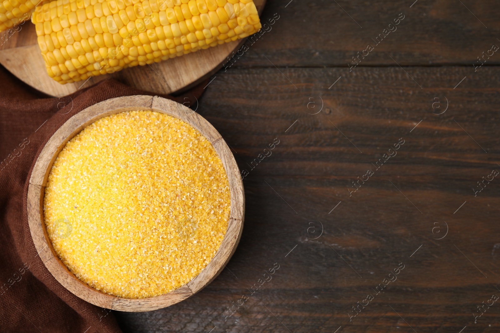 Photo of Raw cornmeal in bowl and corn cob on wooden table, top view. Space for text