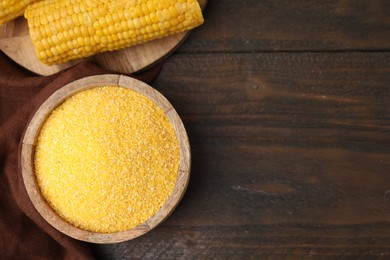 Photo of Raw cornmeal in bowl and corn cob on wooden table, top view. Space for text