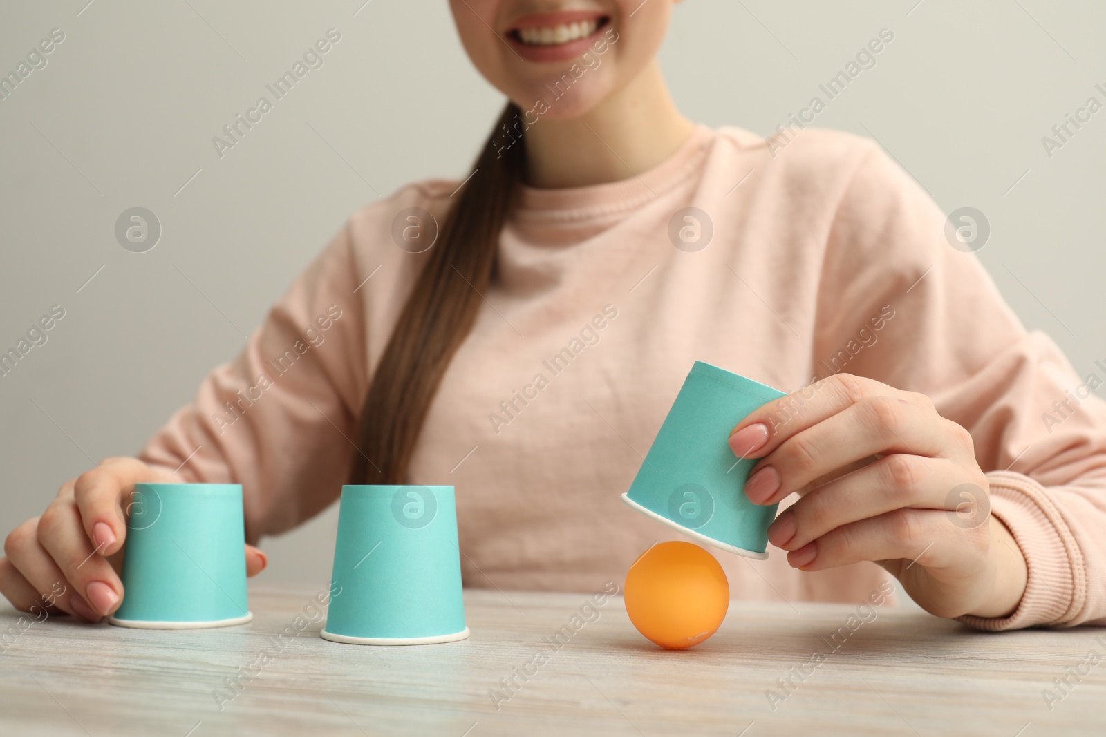 Photo of Shell game. Woman showing ball under cup at wooden table, closeup