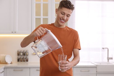 Happy man pouring water from filter jug into glass in kitchen