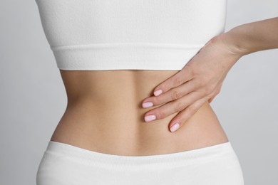 Woman suffering from pain in back on light background, closeup