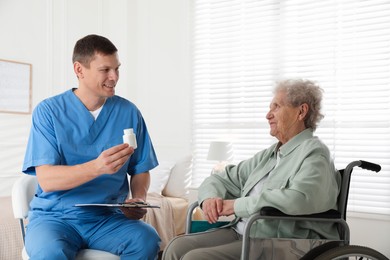 Photo of Caregiver giving medication to senior woman indoors. Home health care service