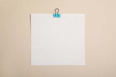 Photo of Sheet of paper with clip on beige background, top view