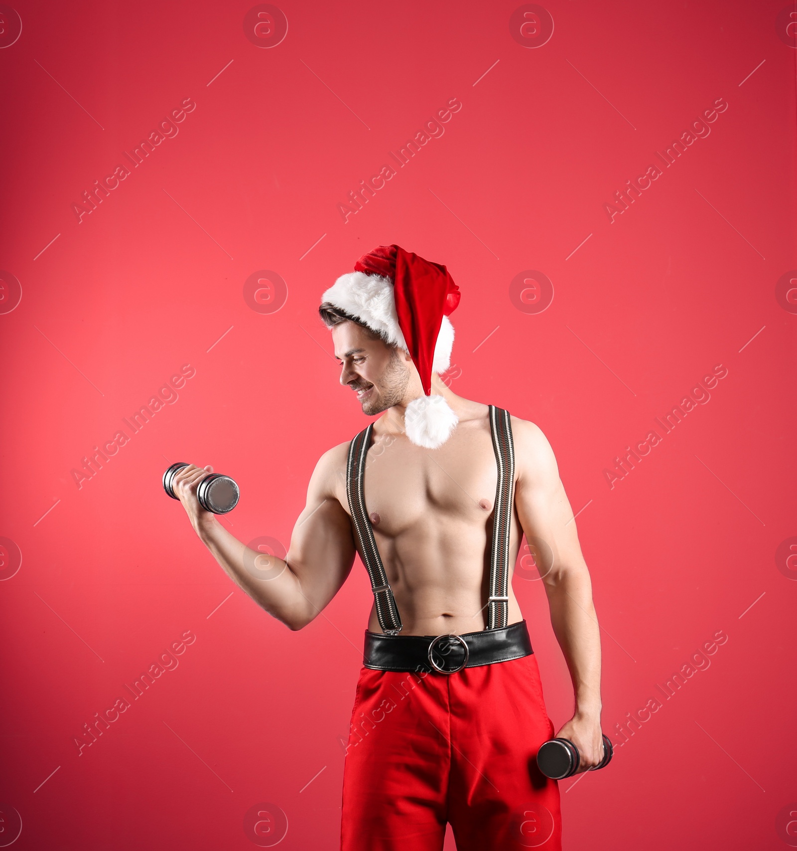 Photo of Shirtless sexy young Santa Claus with dumbbells on color background