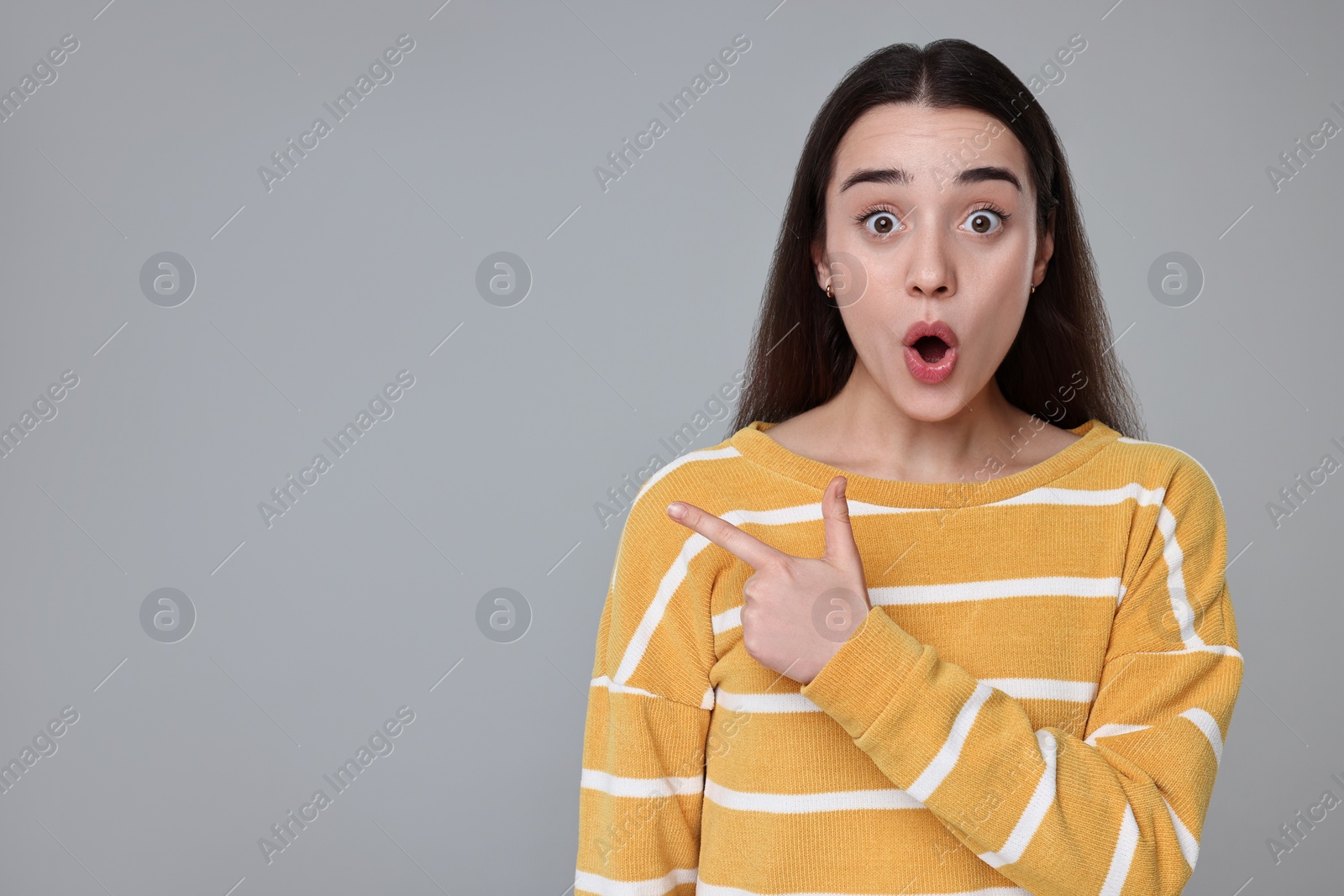 Photo of Portrait of surprised woman pointing at something on grey background. Space for text