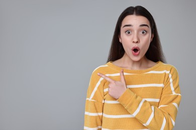 Photo of Portrait of surprised woman pointing at something on grey background. Space for text