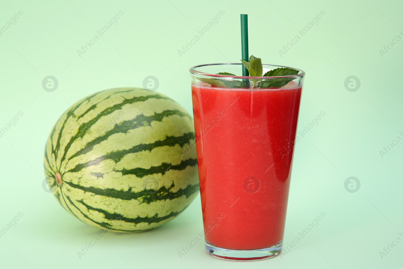 Photo of Glass of delicious drink with mint and fresh watermelon on light green background