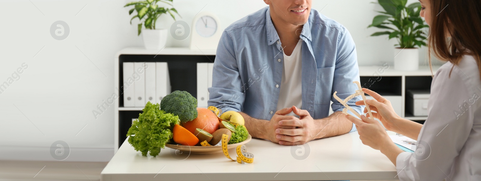 Image of Young nutritionist consulting patient at table in clinic, closeup. Banner design