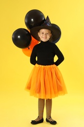 Photo of Cute little girl with balloons wearing Halloween costume on yellow background