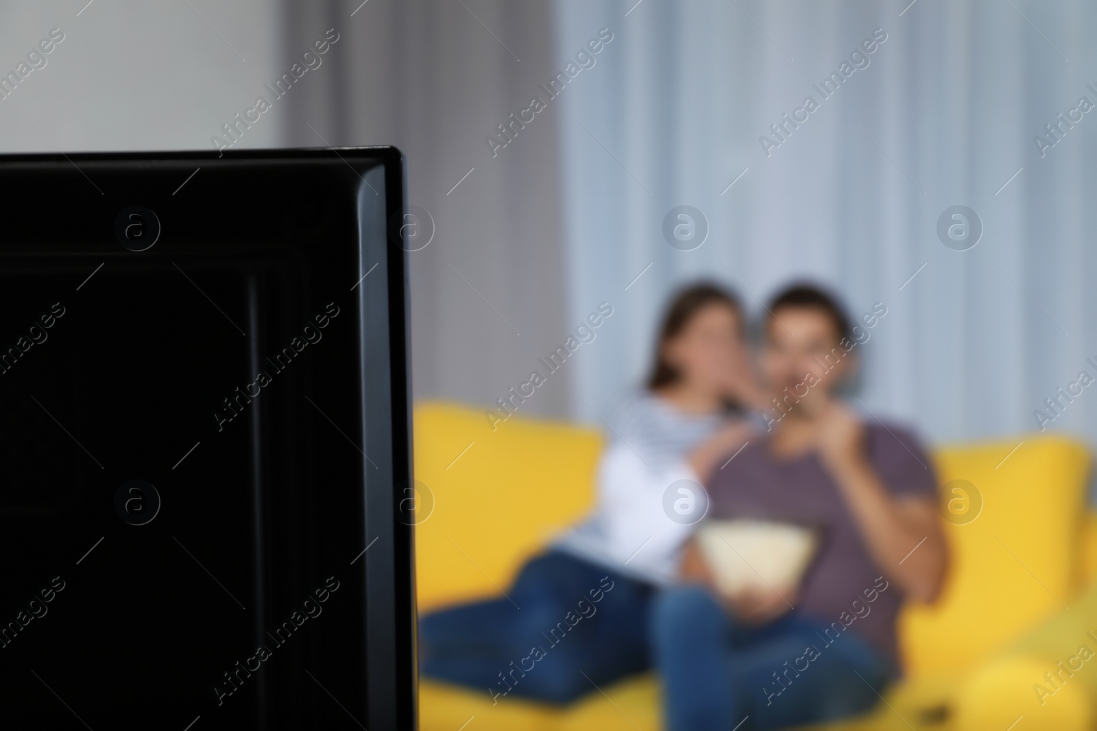 Photo of TV set and blurred couple on background. Space for text