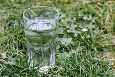 Glass with pure water on green grass outdoors, space for text