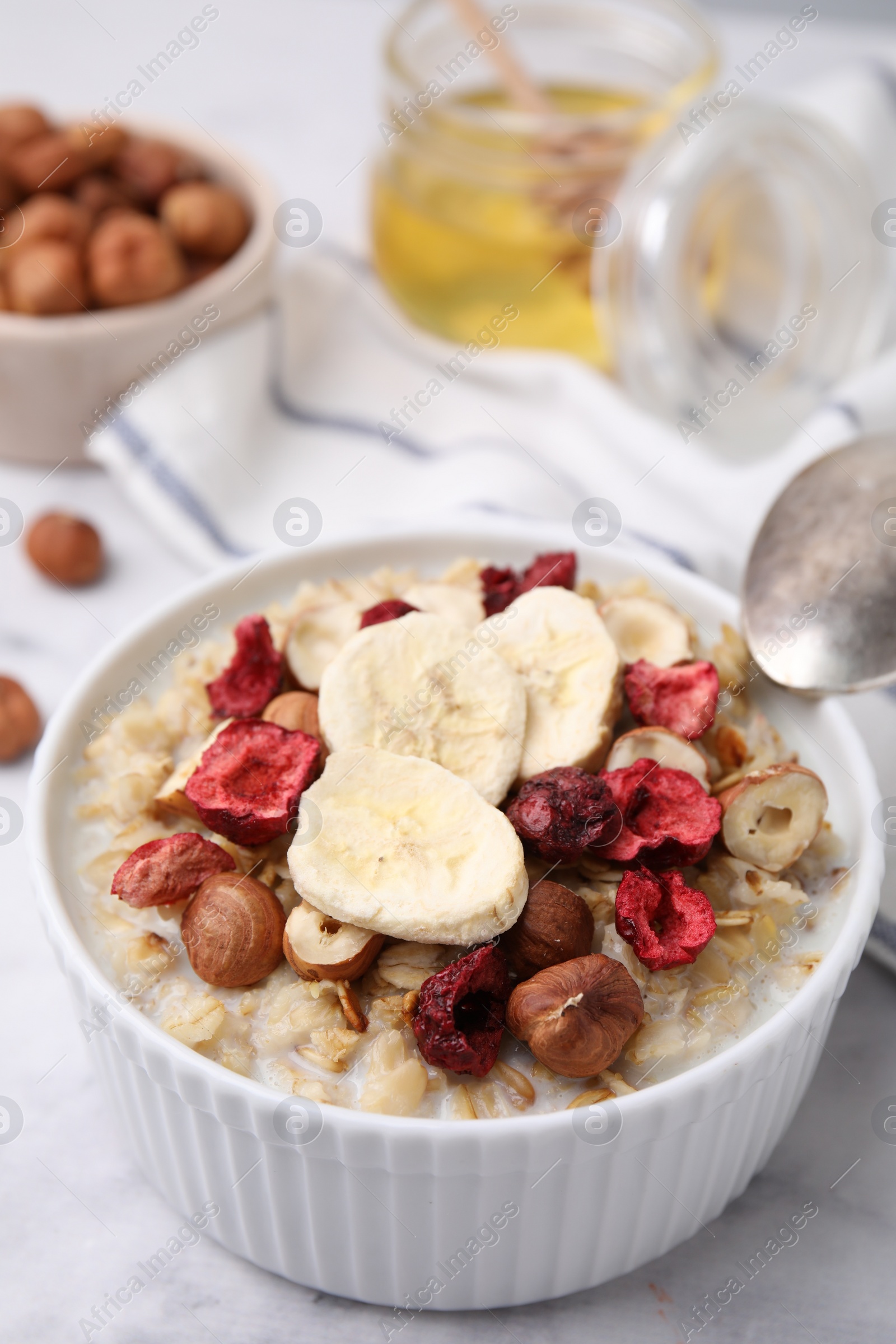 Photo of Delicious oatmeal with freeze dried berries, banana and hazelnuts on white table, closeup