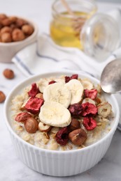 Delicious oatmeal with freeze dried berries, banana and hazelnuts on white table, closeup