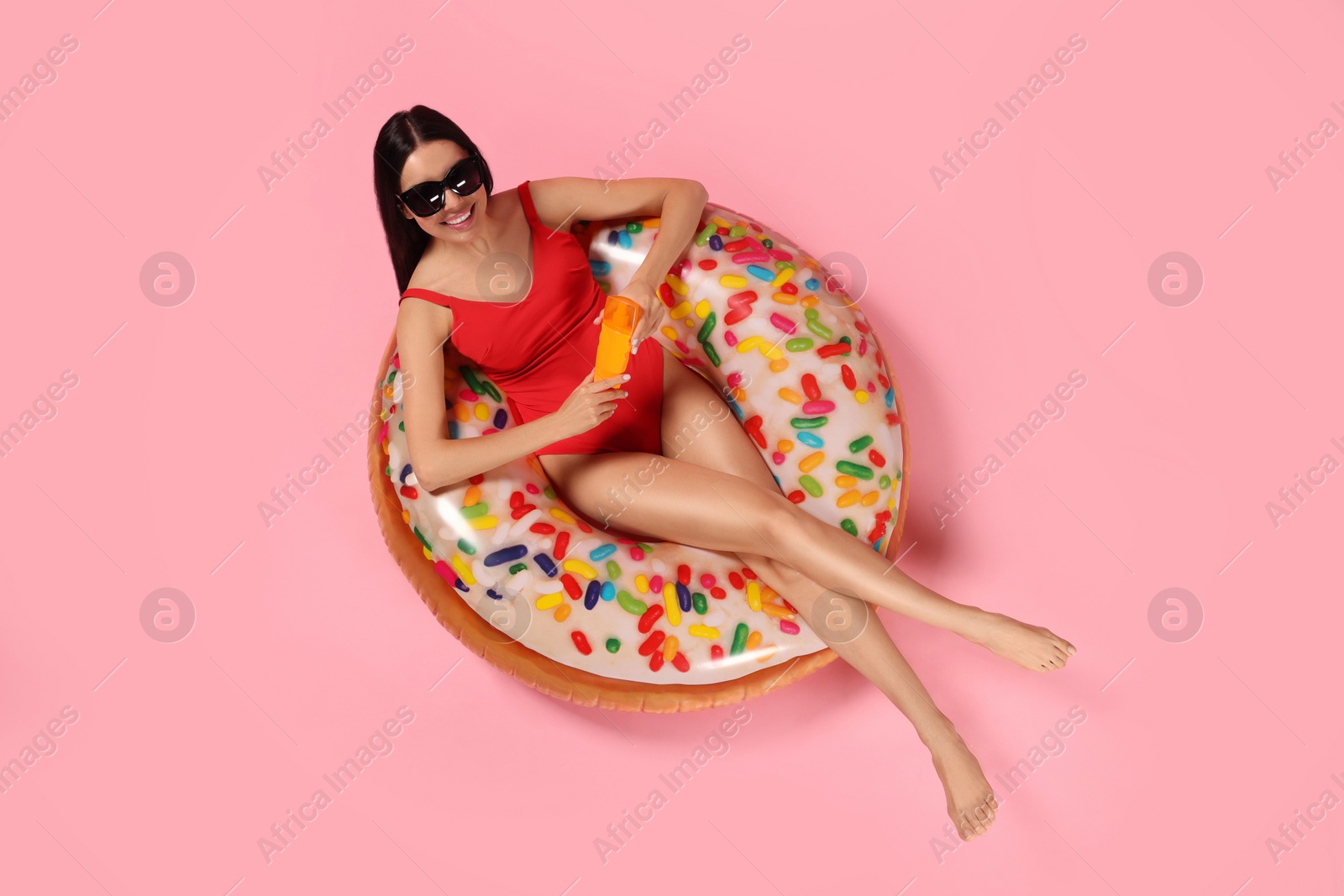 Photo of Young woman with sun protection cream on inflatable ring against pink background, top view