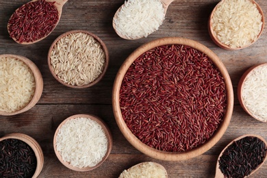 Photo of Flat lay composition with brown and other types of rice in bowls and spoons on wooden table