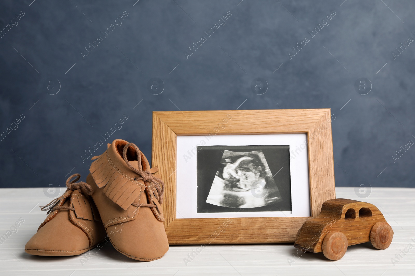 Photo of Composition with child's booties, ultrasound photo and toy on white table