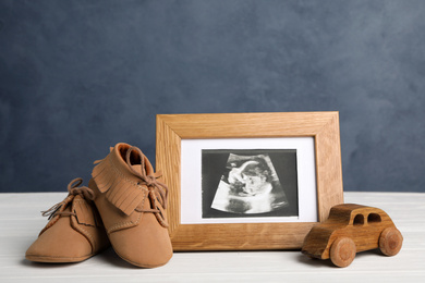 Photo of Composition with child's booties, ultrasound photo and toy on white table