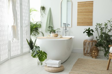 Photo of Stylish bathroom interior with modern tub, houseplants and beautiful decor. Home design