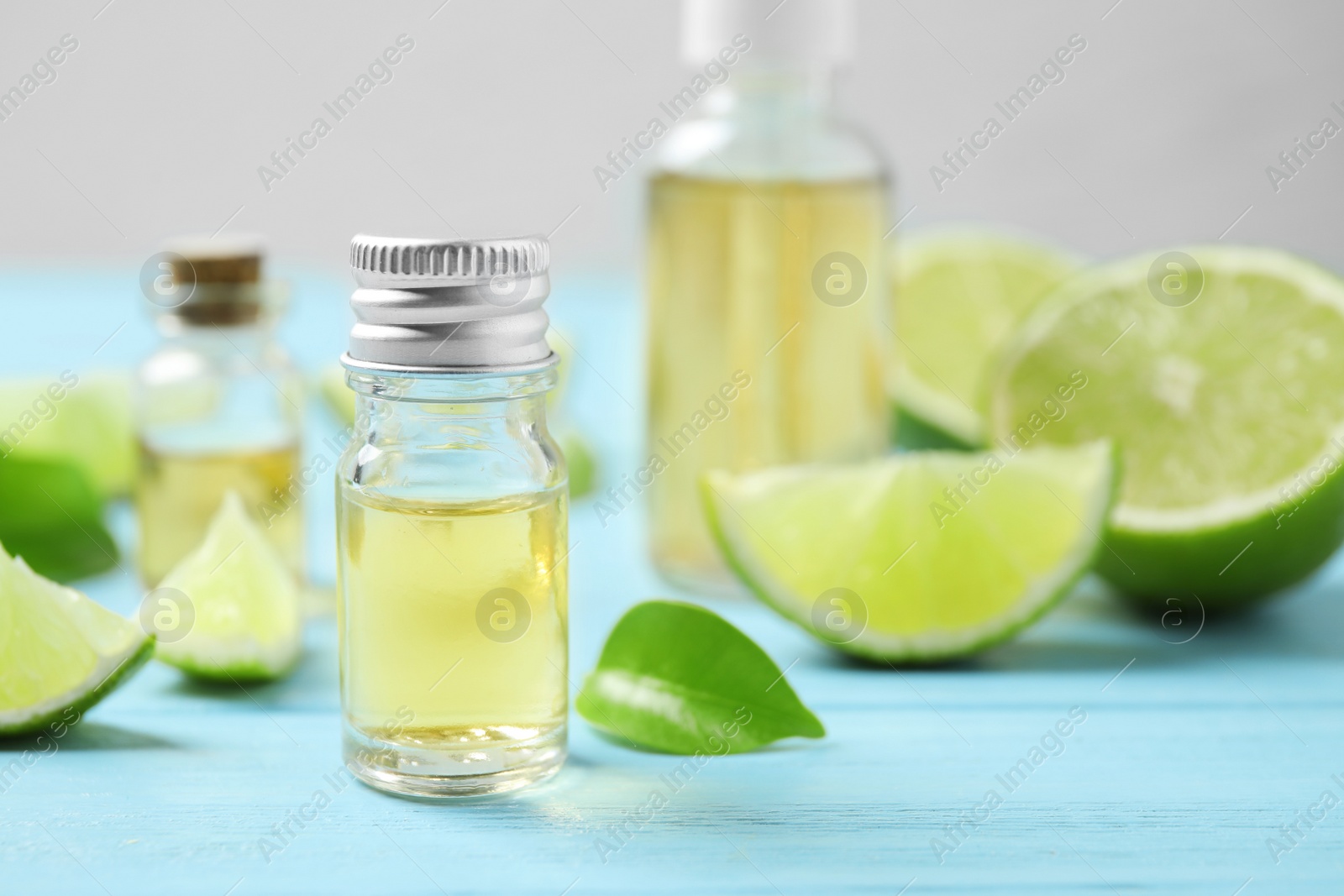 Photo of Lime essential oil and cut citrus fruits on light blue wooden table. Space for text