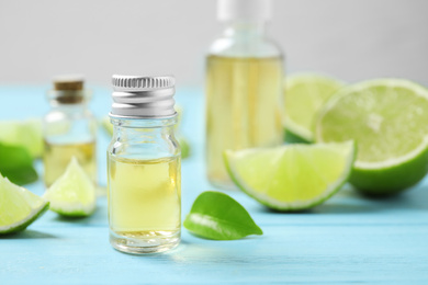 Lime essential oil and cut citrus fruits on light blue wooden table. Space for text