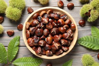 Delicious roasted edible chestnuts on brown wooden table, flat lay