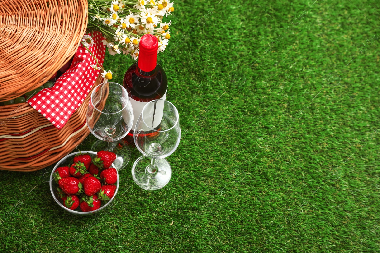 Photo of Picnic basket with wine and bowl of strawberries on grass. Space for text