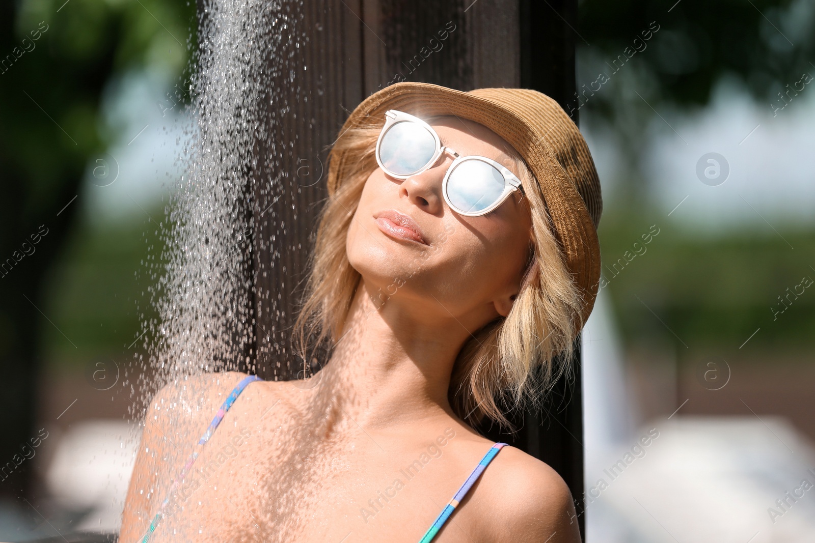 Photo of Sexy young woman with hat and sunglasses taking shower outdoors on sunny day