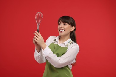 Happy professional confectioner in apron holding whisk on red background