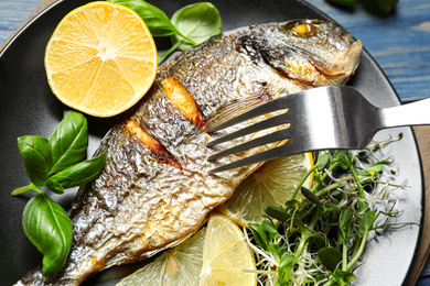Photo of Delicious roasted fish with lemon and greens on plate, closeup